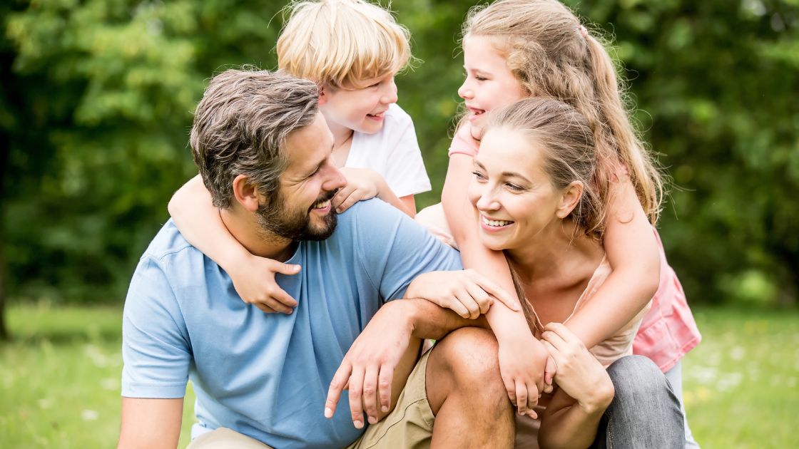 A smiling family sitting together on a couch, looking at a tablet, sharing and enjoying family photos and videos. Emotional Benefits of Storytelling - Every Photo Deserves a Story