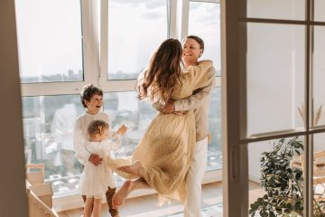 Joyful Homecoming – A mother leaps into her partner’s arms as their children excitedly watch, illustrating the happiness of returning home and cherishing family moments