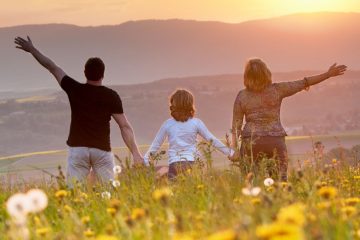 Sunset Family Walk – A family of three holds hands while gazing at the golden sunset in a field of flowers, symbolizing togetherness, nostalgia, and the beauty of shared moments
